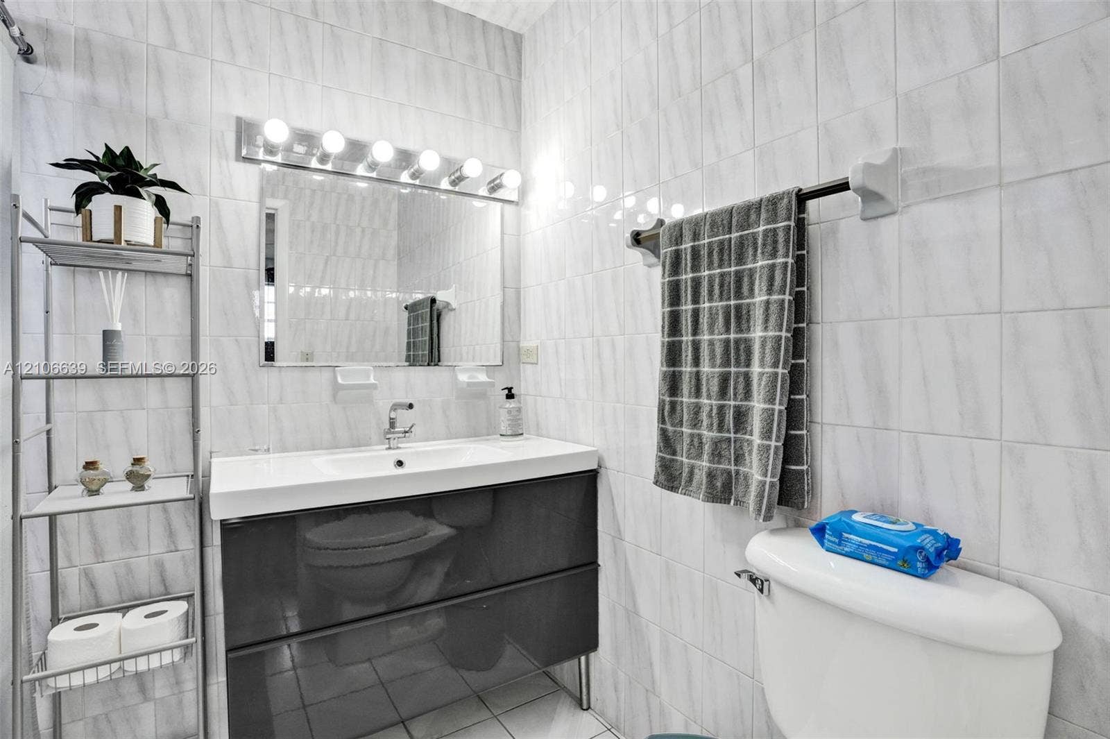 Wall-to-wall tiled surfaces, vanity with a rectangular basin, high-gloss cabinetry, and multi-bulb linear vanity lighting