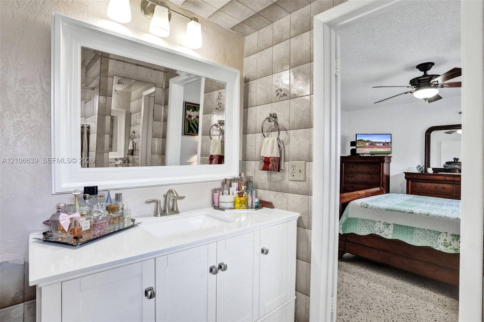Bathroom vanity with white cabinetry, solid surface countertop, rectangular undermount sink, three-light fixture, and framed wall mirror, accompanied by tiled walls