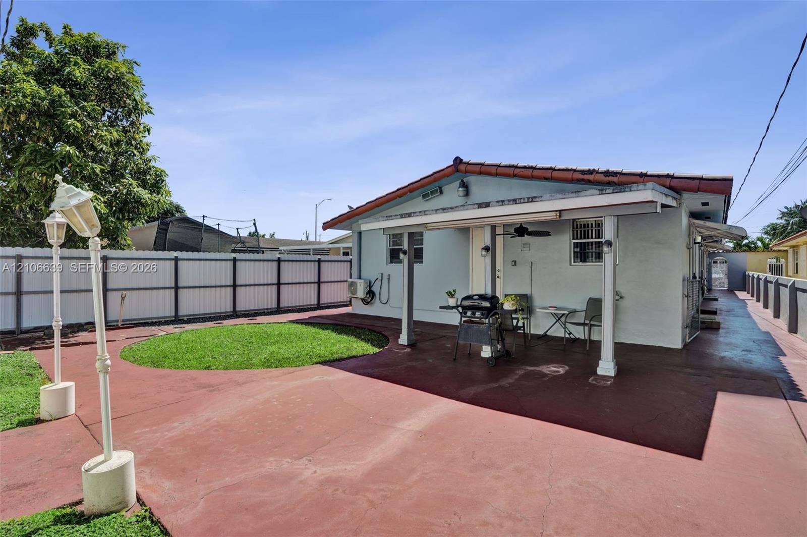 Backyard featuring a covered patio, concrete hardscaping, white vinyl privacy fencing, and a built-in outdoor lighting fixture