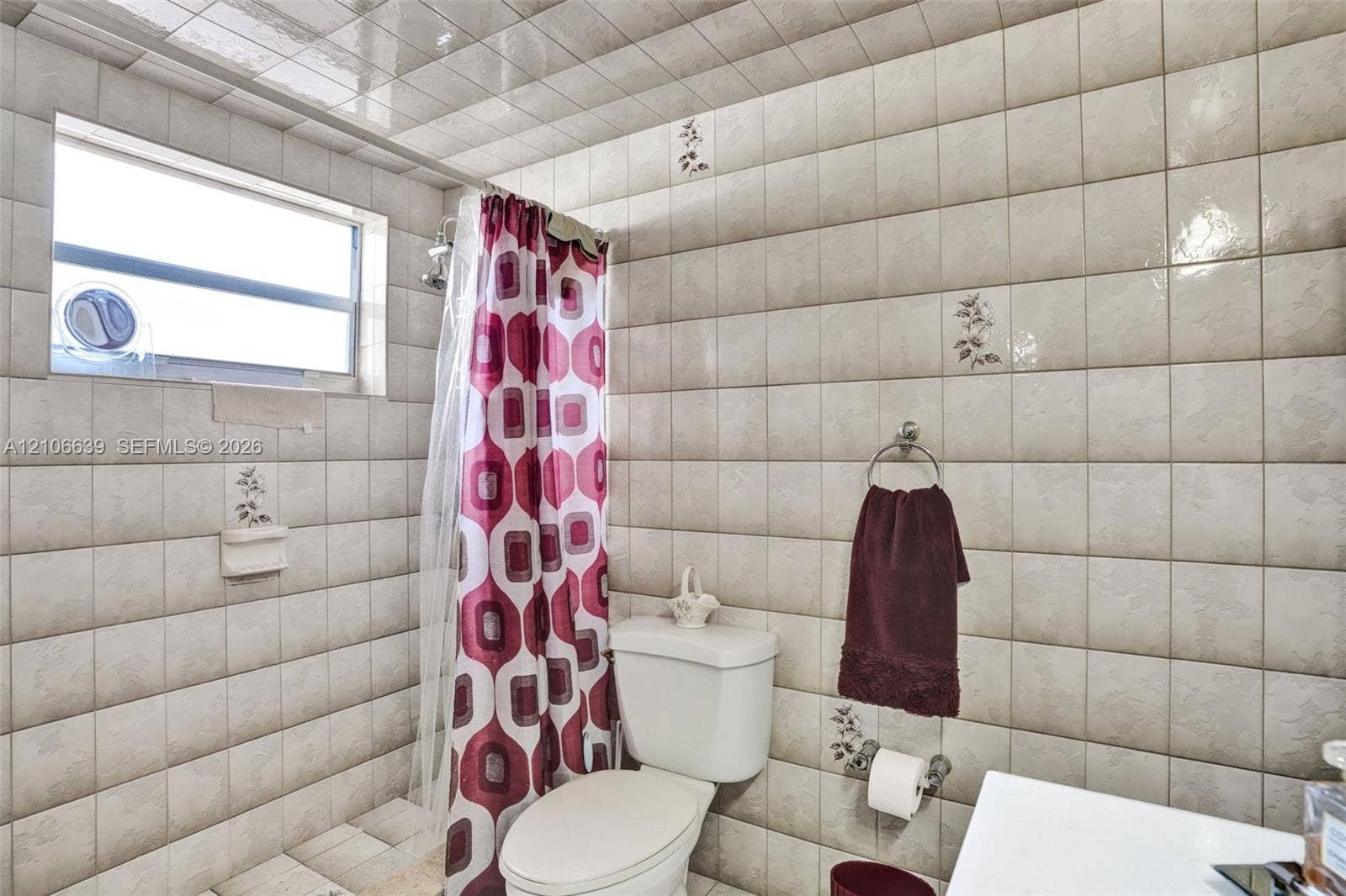 Full-height ceramic wall tiling, high-gloss ceiling tiles, integrated soap dish, and a horizontal window