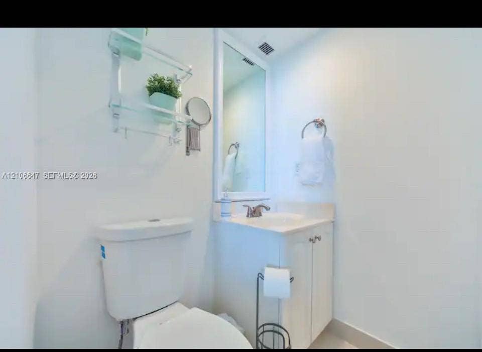 Bathroom featuring a white vanity cabinet with a stone-top integrated sink, a framed wall mirror, and a wall-mounted glass shelving unit