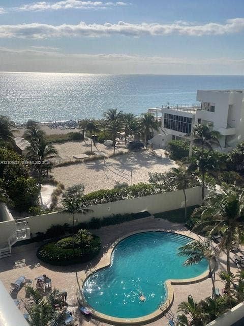 Free-form swimming pool with paved surround, lush perimeter landscaping, and direct access to sand-covered grounds