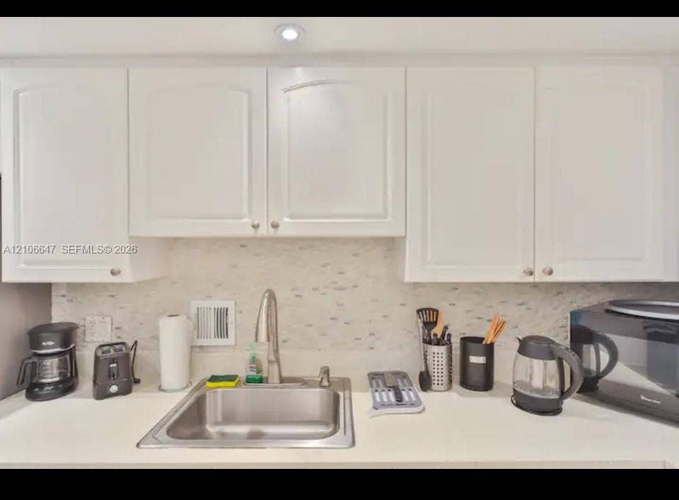 White shaker-style cabinetry, solid-surface countertop, stainless steel undermount sink, gooseneck faucet, and mosaic tile backsplash