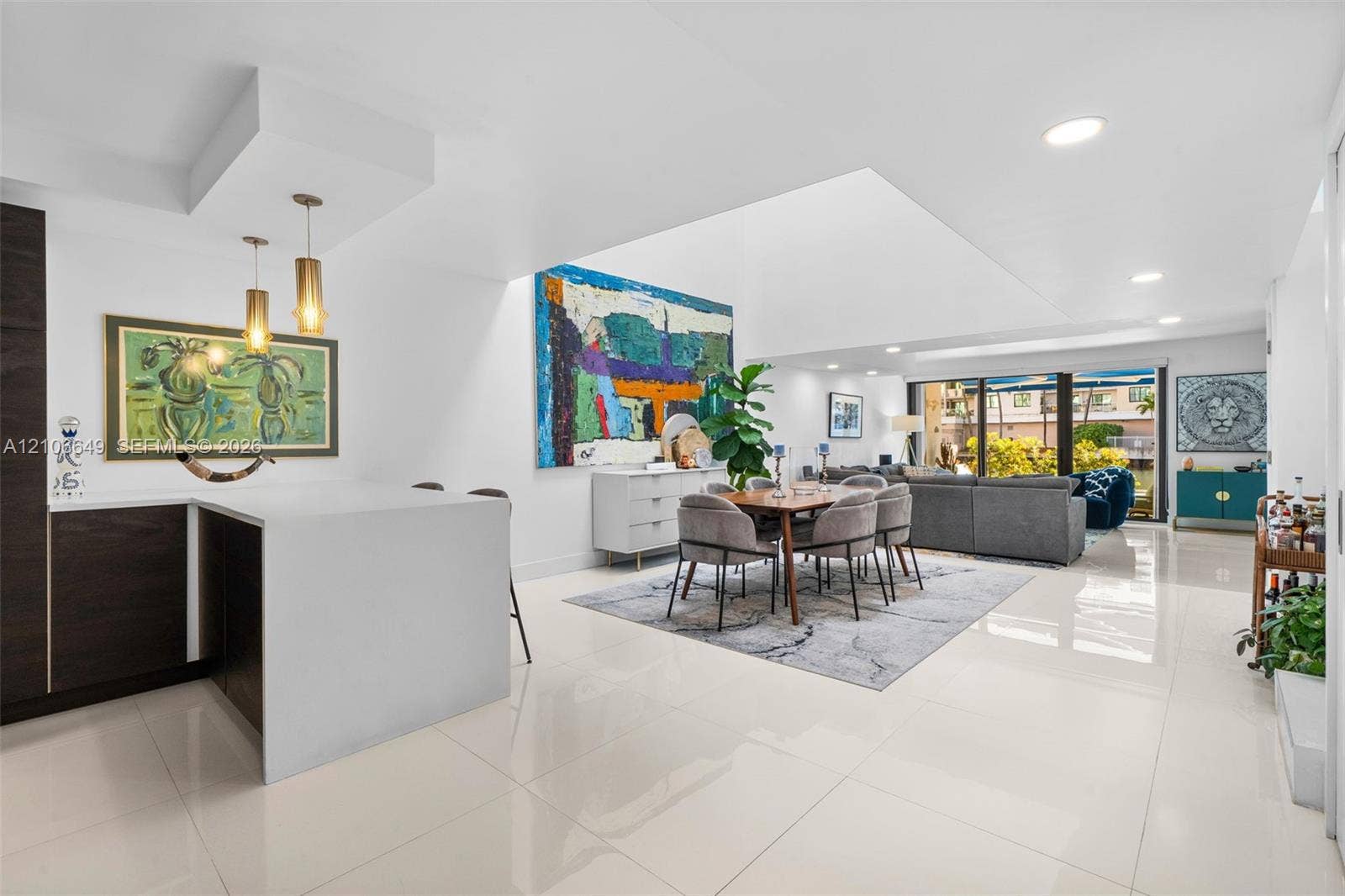 216 Poinciana Drive, #206, Sunny Isles Beach, FL 33160 Open-concept living space featuring white polished tile flooring, recessed ceiling lighting, a waterfall-edge kitchen island, dual pendant lights, and large sliding glass doors