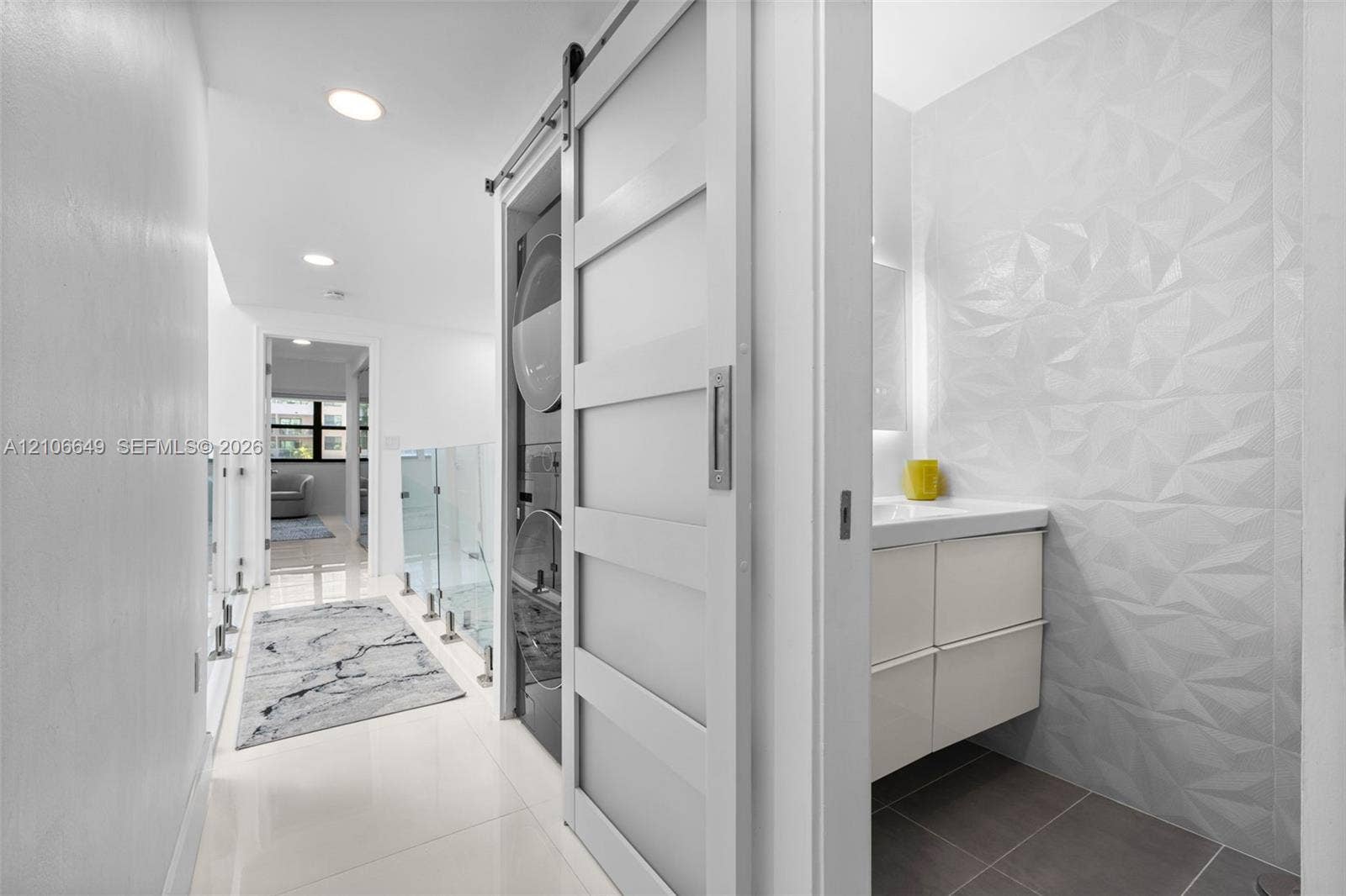 216 Poinciana Drive, #206, Sunny Isles Beach, FL 33160 Sliding door entry concealing stacked laundry appliances, textured geometric wall tiling, modern wall-mounted vanity, and glass panel railing