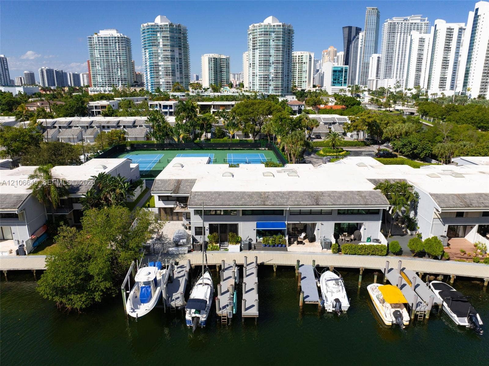 216 Poinciana Drive, #206, Sunny Isles Beach, FL 33160 Waterfront residential complex featuring private boat slips, hardscaped docks, a multi-court tennis facility, and expansive coastal surroundings