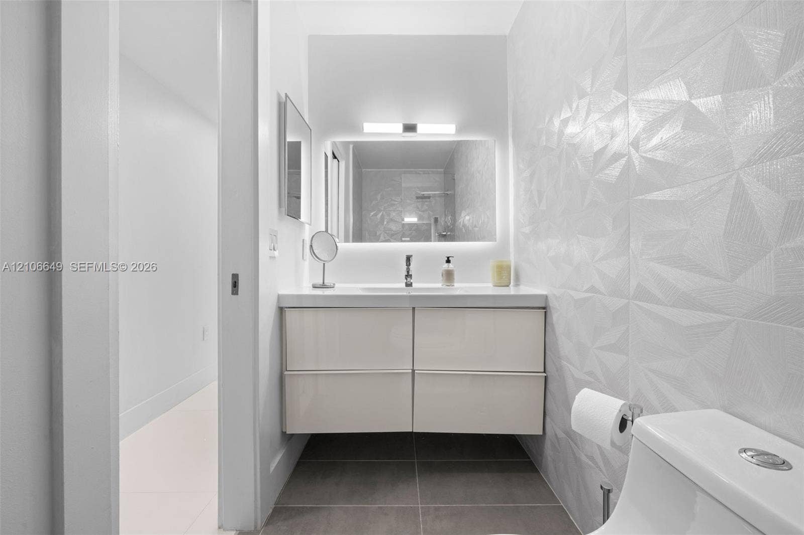 216 Poinciana Drive, #206, Sunny Isles Beach, FL 33160 Floating vanity with a smooth-finish countertop, integrated under-mount sink, geometric textured tile walls, and a backlit mirror