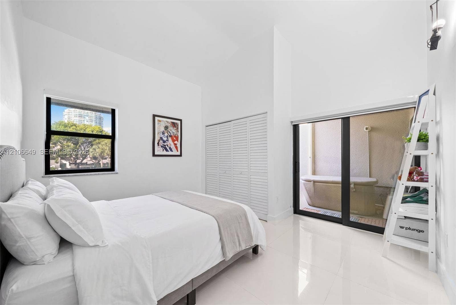 216 Poinciana Drive, #206, Sunny Isles Beach, FL 33160 High-ceiling room featuring white tile flooring, louvered-panel closet doors, and a large sliding glass door with access to an exterior area