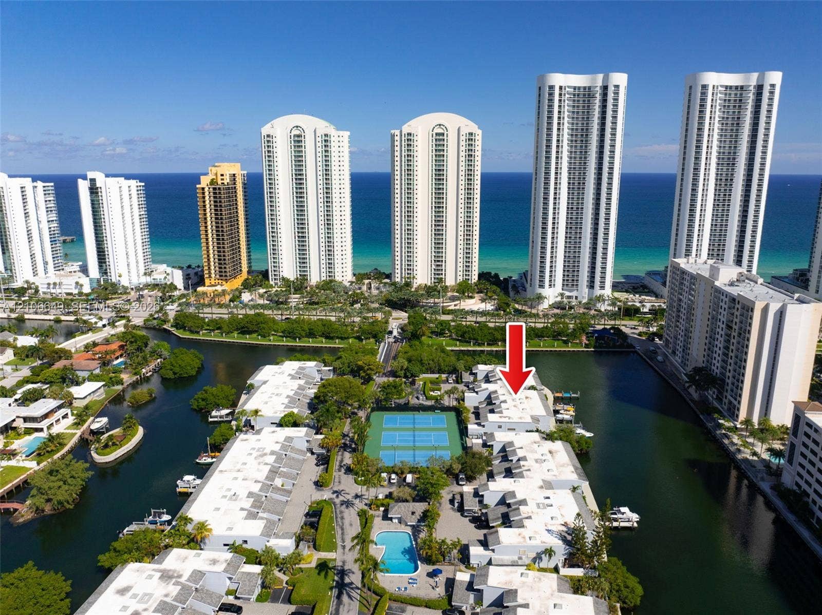 216 Poinciana Drive, #206, Sunny Isles Beach, FL 33160 Aerial perspective of a multi-unit property complex featuring tennis courts, a swimming pool, and direct canal access