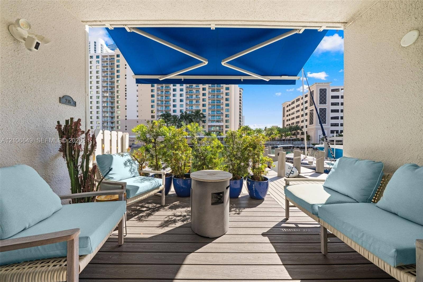 216 Poinciana Drive, #206, Sunny Isles Beach, FL 33160 Covered balcony featuring wood-finish composite decking, a retractable fabric awning, and integrated wall-mounted lighting