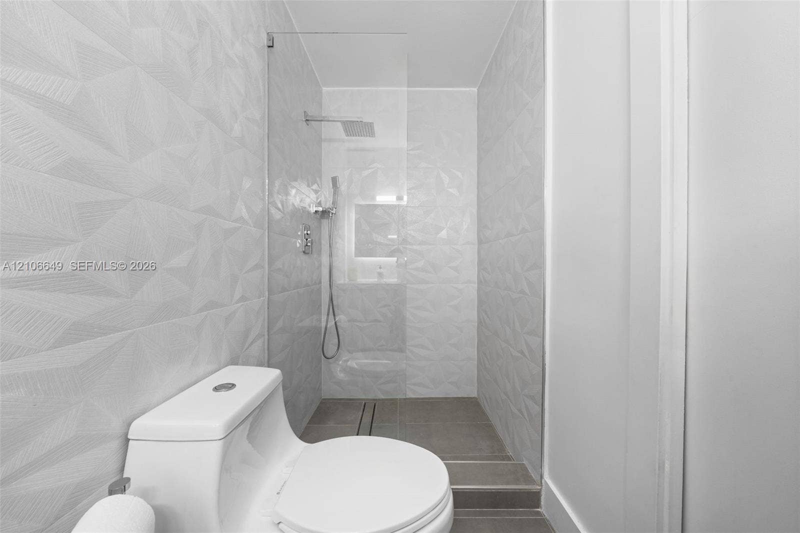 216 Poinciana Drive, #206, Sunny Isles Beach, FL 33160 Walk-in shower featuring textured geometric wall tile, a frameless glass enclosure, a rainfall showerhead, and a built-in recessed niche