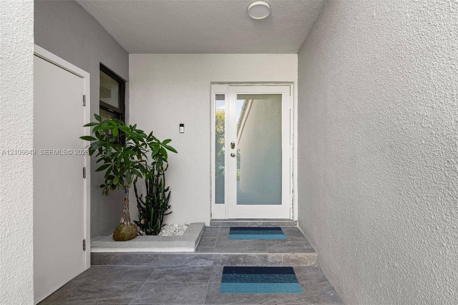 216 Poinciana Drive, #206, Sunny Isles Beach, FL 33160 Entryway featuring a white door with a frosted glass panel, recessed ceiling lighting, textured wall finish, grey tiled flooring, and a built-in stone planter