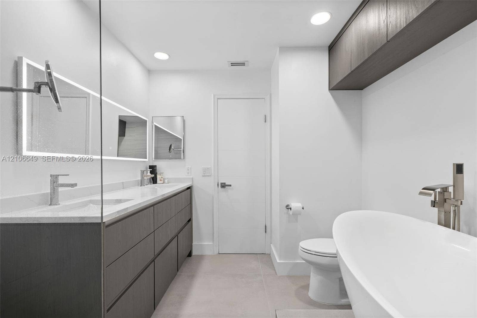 216 Poinciana Drive, #206, Sunny Isles Beach, FL 33160 Modern dual vanity with stone countertop, freestanding soaking tub, wall-mounted faucets, and dark wood-finish cabinetry