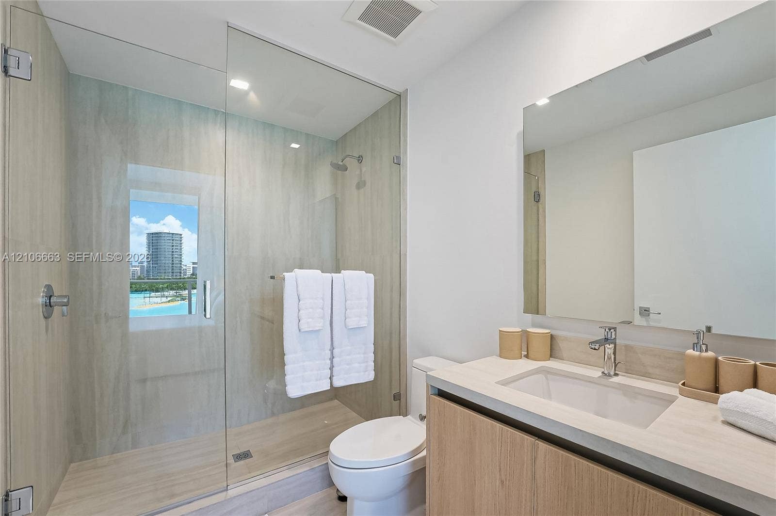 Walk-in shower with floor-to-ceiling tile, frameless glass enclosure, wood-finish cabinetry, countertop vanity with integrated sink, and polished chrome hardware