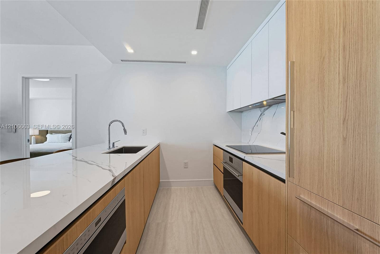 Contemporary kitchen featuring white flat-panel upper cabinetry, light wood-finish lower cabinetry, stone-style countertops with integrated backsplash, built-in cooktop, and undermount stainless steel sink with gooseneck faucet