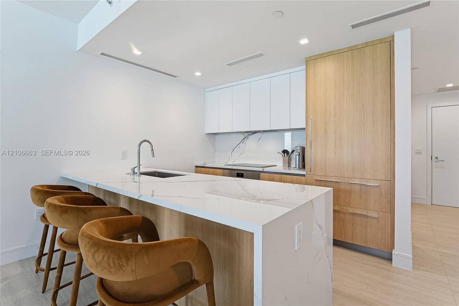 Kitchen featuring waterfall-edge stone countertops, custom cabinetry with wood-finish paneling, integrated refrigerator, stone backsplash, and stainless-steel sink with a gooseneck faucet