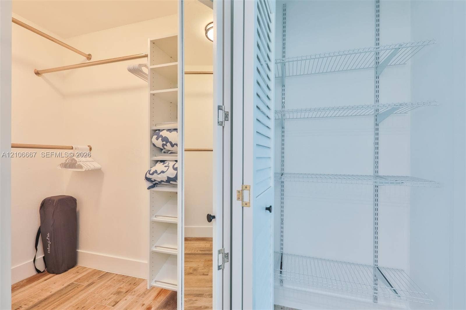 209 Bayshore Drive, Cape Coral, FL 33904 Walk-in closet featuring wood-finish flooring, built-in shelving tower, tiered hanging rods, and a separate pantry-style storage area with louvered doors and wire shelving