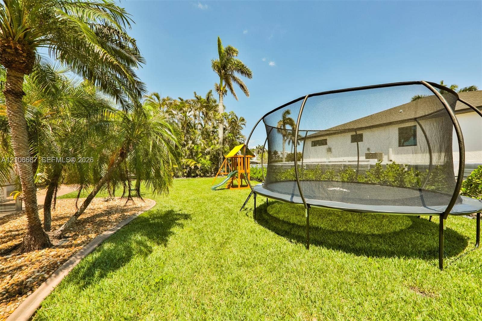 209 Bayshore Drive, Cape Coral, FL 33904 Fenced backyard featuring a manicured lawn, mature palm trees, and perimeter landscaping