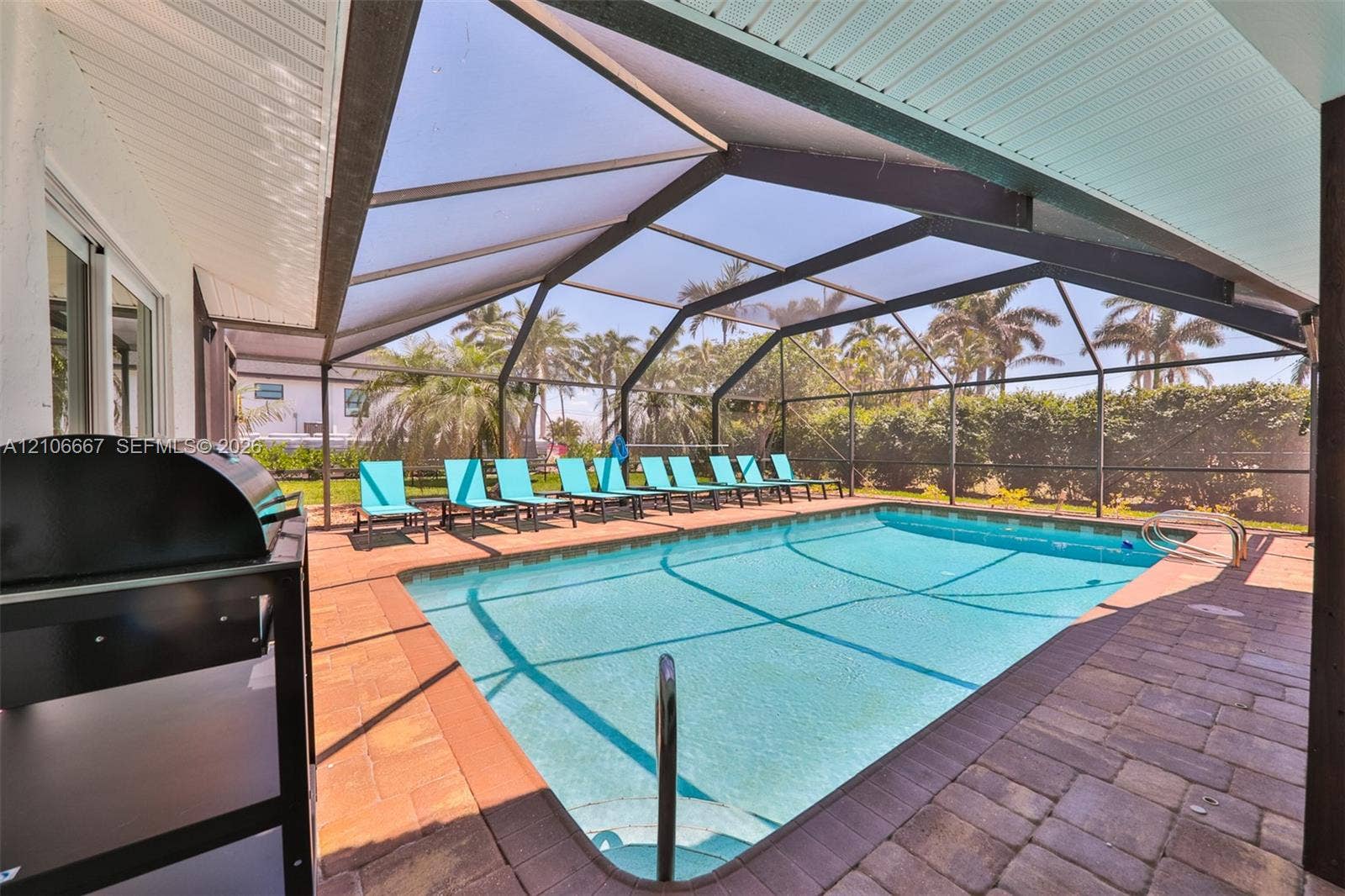 209 Bayshore Drive, Cape Coral, FL 33904 Screened-in pool enclosure featuring paver decking, a built-in pool with metal ladder, and a covered patio area