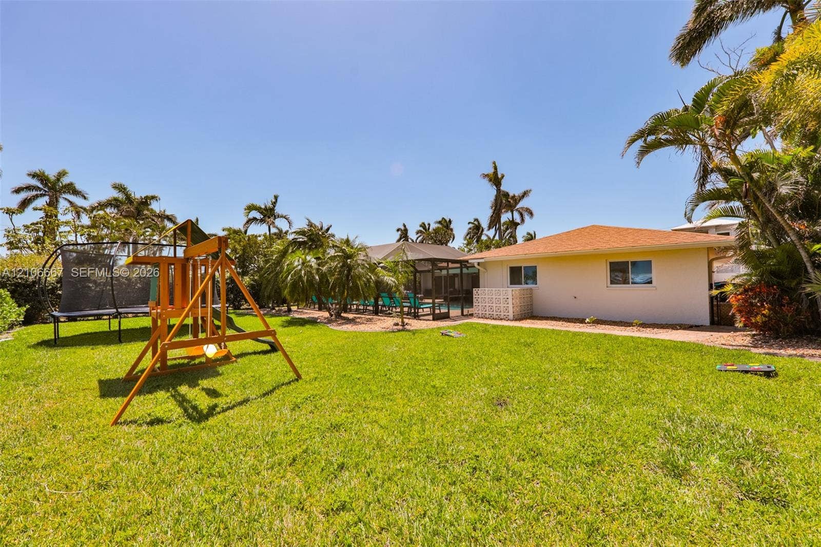 209 Bayshore Drive, Cape Coral, FL 33904 Expansive backyard featuring a manicured lawn, established palm trees, a screened-in lanai, and an exterior masonry privacy wall