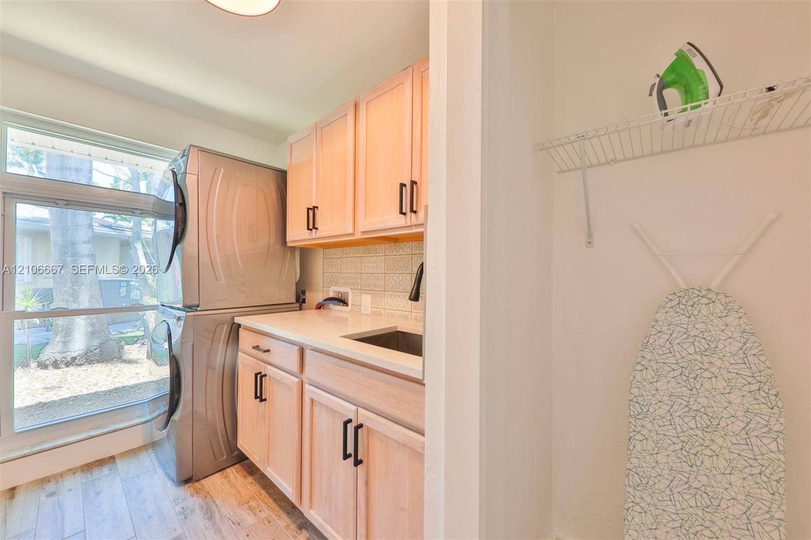 209 Bayshore Drive, Cape Coral, FL 33904 Utility room featuring light-finish cabinetry, a white countertop with an integrated sink, a ceramic tile backsplash, and wood-finish flooring