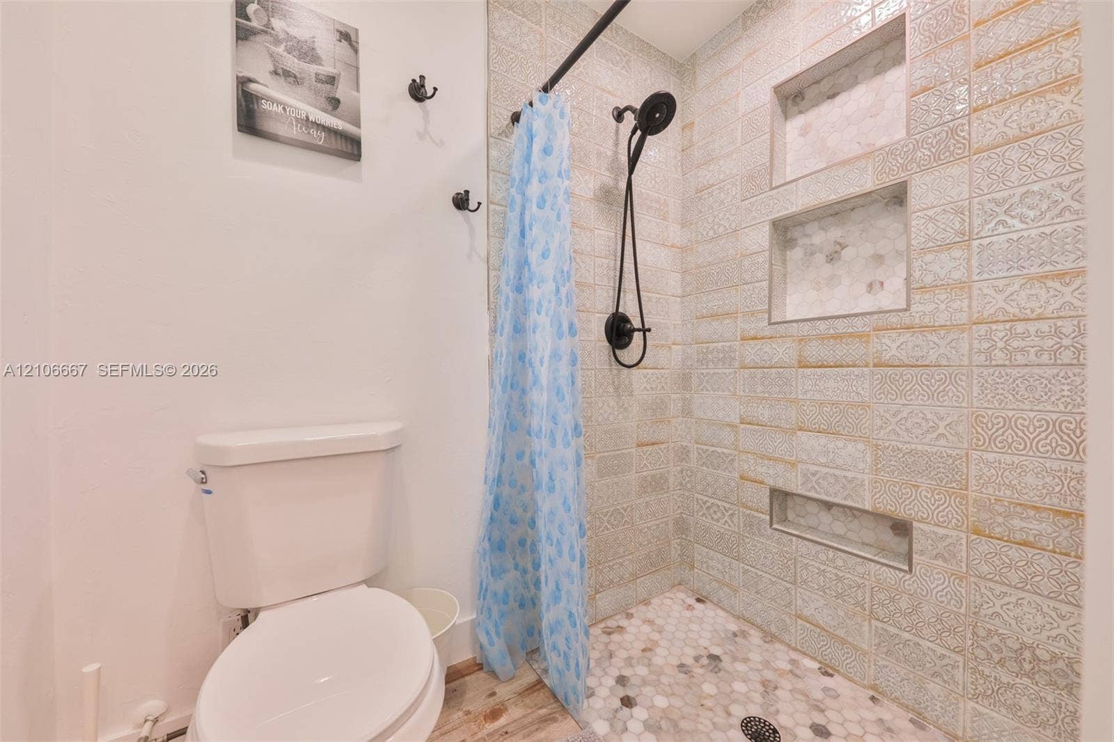 209 Bayshore Drive, Cape Coral, FL 33904 Bathroom featuring textured tile shower walls with three built-in wall niches, a hexagonal mosaic stone shower floor, matte black shower hardware, and a white porcelain toilet
