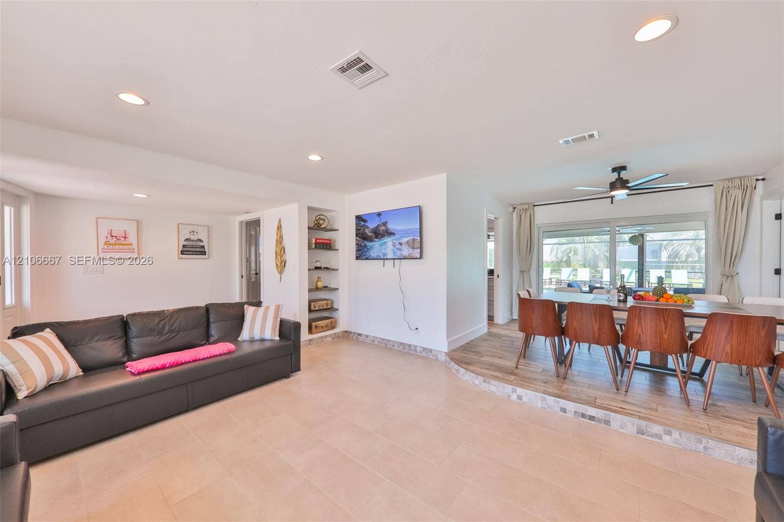 209 Bayshore Drive, Cape Coral, FL 33904 Open-concept interior featuring light-toned tile flooring, recessed lighting, built-in wall shelving, wood-finish raised platform, and large sliding glass doors