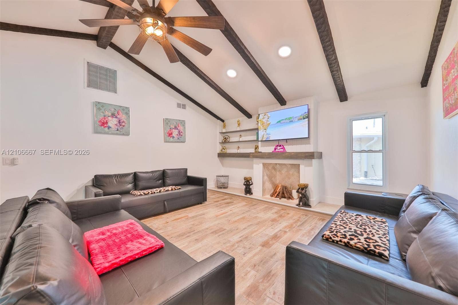 209 Bayshore Drive, Cape Coral, FL 33904 Vaulted ceiling featuring exposed dark wood beams, wood-finish flooring, masonry fireplace with a timber mantel, and built-in shelving