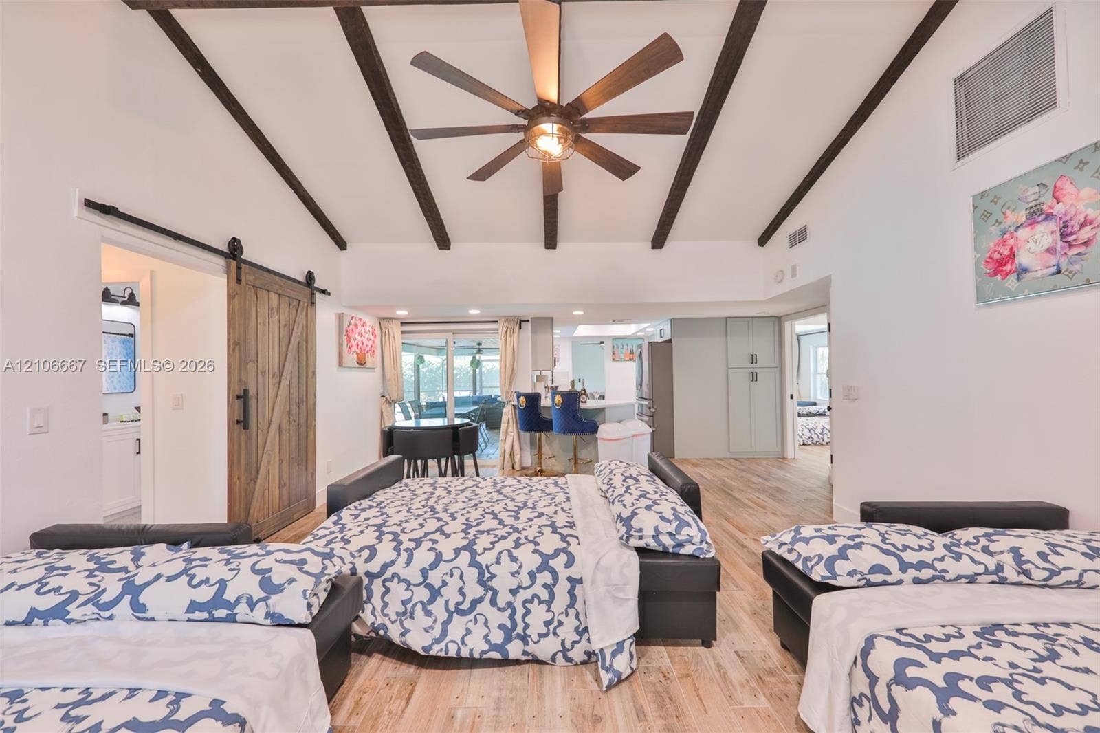 209 Bayshore Drive, Cape Coral, FL 33904 Vaulted ceiling with exposed decorative beams, wood-finish flooring, sliding barn door with matte black hardware, and central ceiling fan with integrated light fixture