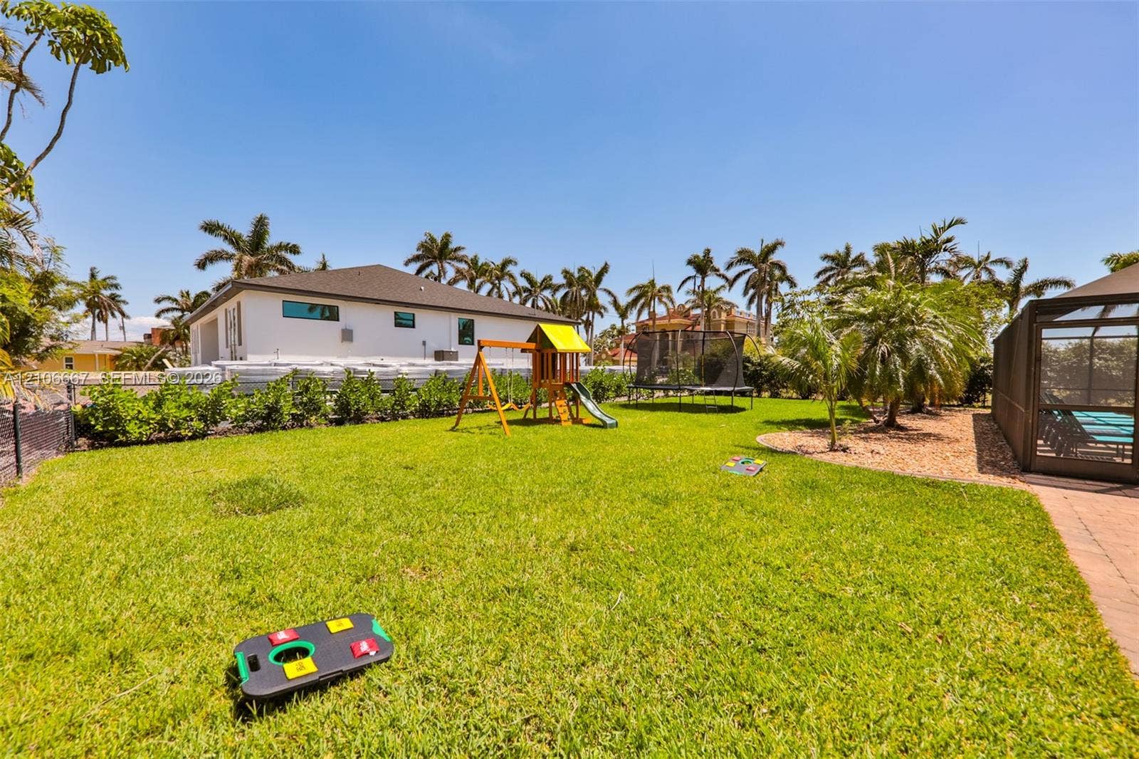 209 Bayshore Drive, Cape Coral, FL 33904 Expansive backyard featuring a manicured lawn, established palm trees, a paver patio, and a screened-in enclosure