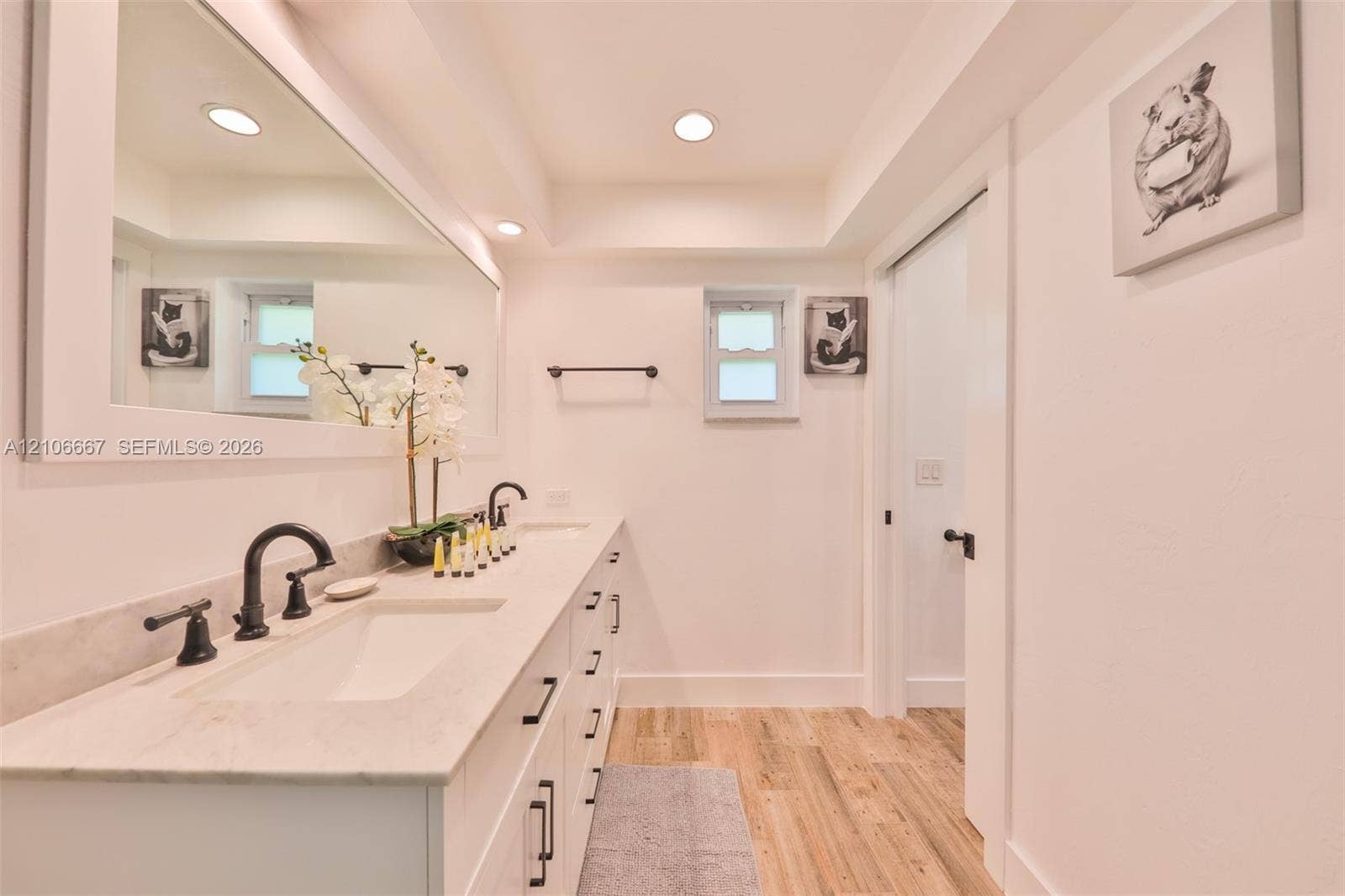 209 Bayshore Drive, Cape Coral, FL 33904 Double vanity featuring a light-toned countertop with dual integrated sinks, matte black widespread faucets, full-width framed mirror, and wood-finish flooring