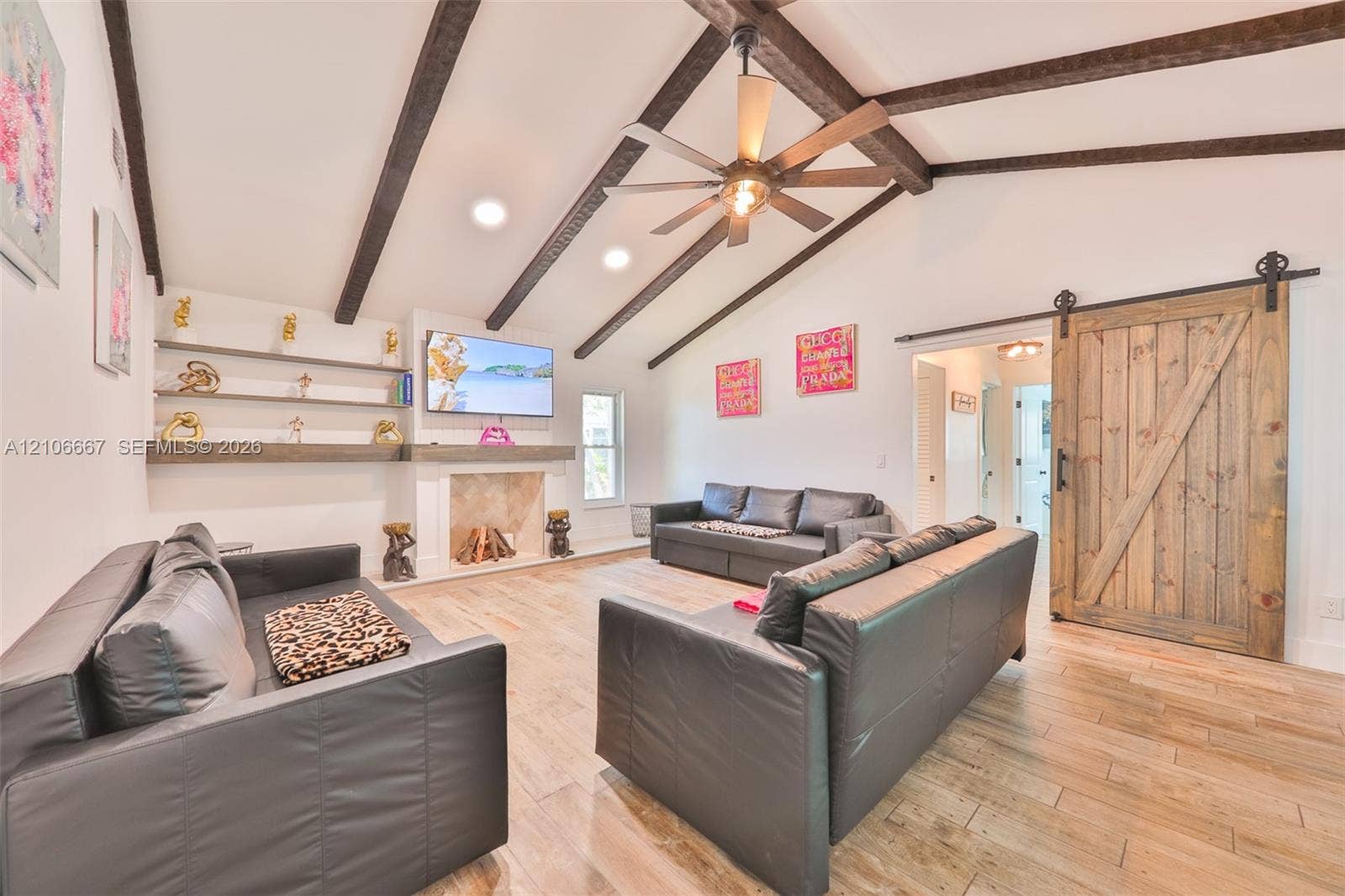 209 Bayshore Drive, Cape Coral, FL 33904 Vaulted ceiling featuring exposed wood beams, wood-finish flooring, fireplace with stone surround, custom built-in shelving, and sliding barn-style door