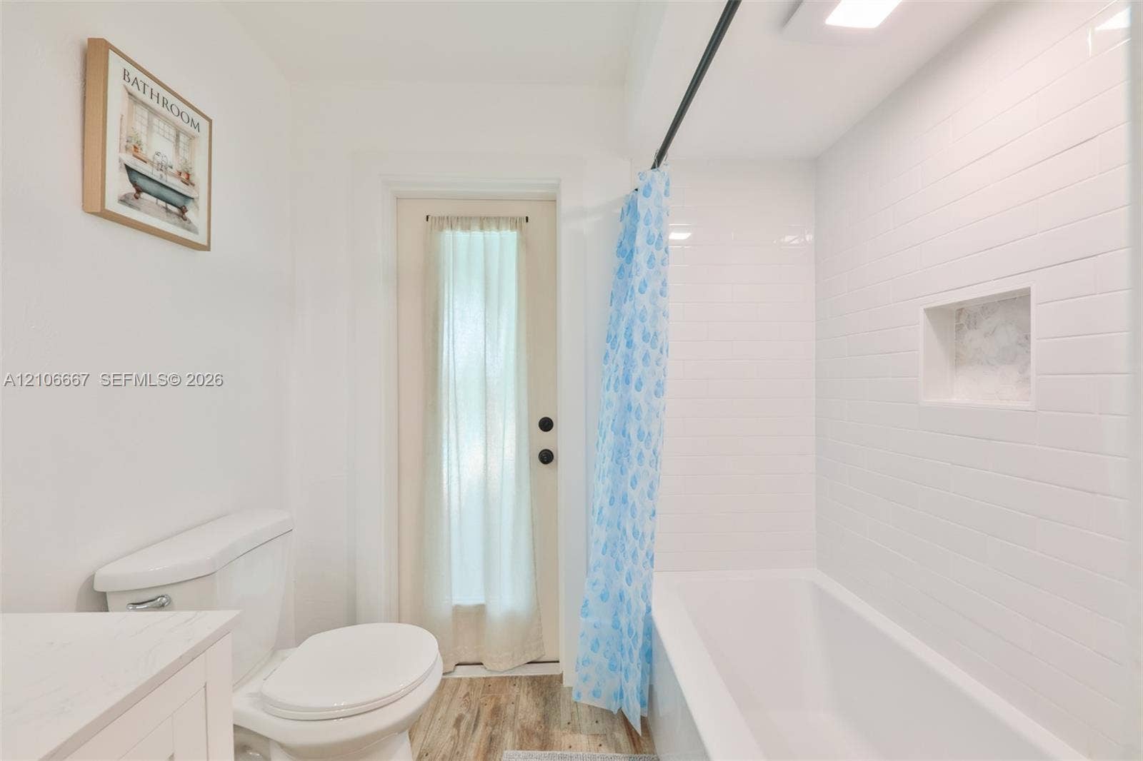 209 Bayshore Drive, Cape Coral, FL 33904 Bathroom featuring a tub with white subway tile surround, built-in recessed wall niche, wood-finish flooring, and a single-door exterior entry