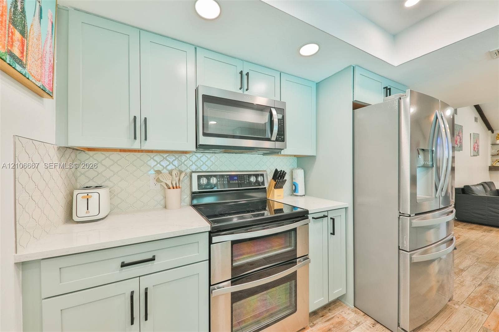 209 Bayshore Drive, Cape Coral, FL 33904 Kitchen featuring light blue cabinetry, stainless steel appliances, quartz countertops, arabesque-pattern tile backsplash, and wood-finish flooring