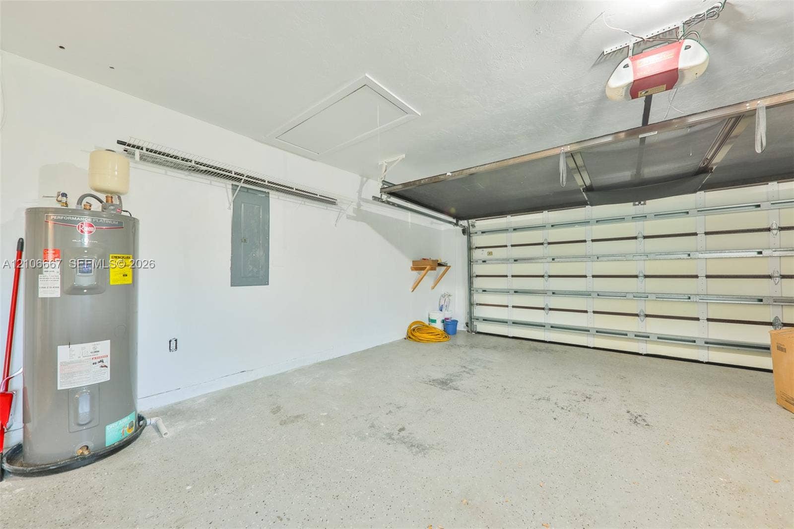 209 Bayshore Drive, Cape Coral, FL 33904 Garage interior featuring a sectional roll-up door, integrated door opener, concrete flooring, and an installed water heater