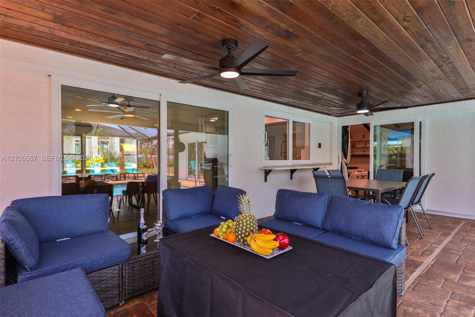 209 Bayshore Drive, Cape Coral, FL 33904 Covered patio featuring a wood-plank ceiling, matte black ceiling fans, paver flooring, sliding glass wall panels, and a built-in exterior pass-through window