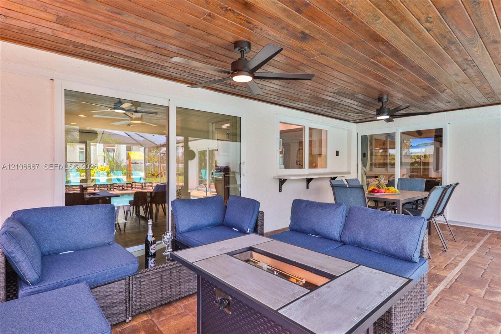 209 Bayshore Drive, Cape Coral, FL 33904 Covered outdoor patio featuring a wood-plank ceiling, paver flooring, dual ceiling fans, and an exterior pass-through window with a built-in counter