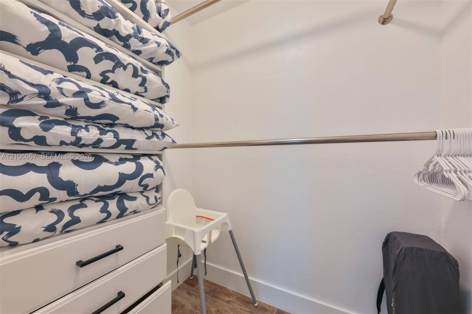 209 Bayshore Drive, Cape Coral, FL 33904 Walk-in closet featuring built-in cabinetry with matte black hardware, dual-tier metal garment rods, and wood-finish flooring