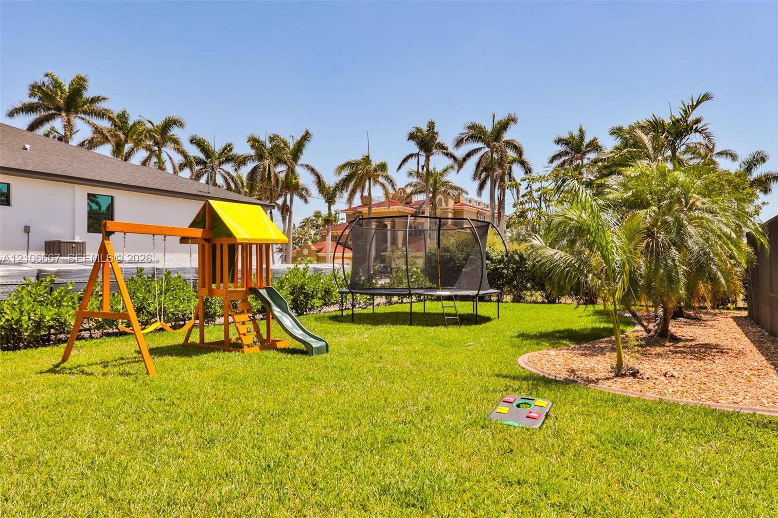 209 Bayshore Drive, Cape Coral, FL 33904 Backyard space featuring a manicured lawn, perimeter landscaping, and mature palm trees