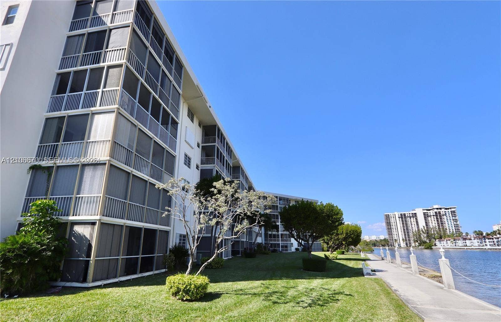 3030 Marcos Drive, #T512, Aventura, FL 33160 Multi-story building exterior featuring screened-in balconies, concrete walkway, manicured lawn, and water frontage