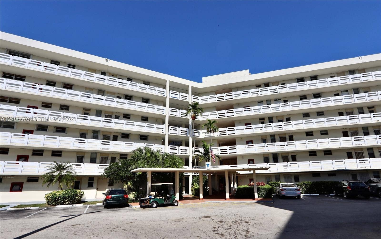 3030 Marcos Drive, #T512, Aventura, FL 33160 Multi-story building exterior featuring white concrete balconies with geometric railings, a covered porte-cochre entry, and mature palm tree landscaping