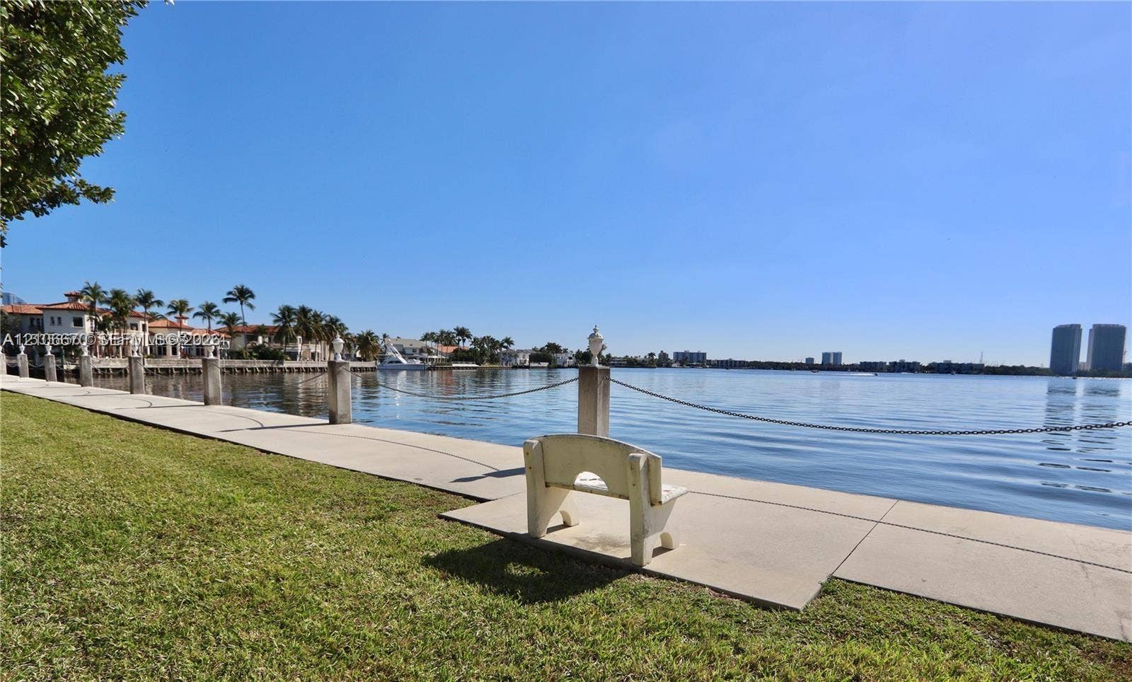 3030 Marcos Drive, #T512, Aventura, FL 33160 Waterfront property featuring a concrete seawall, decorative stone pillars with chain-link railing, and manicured lawn