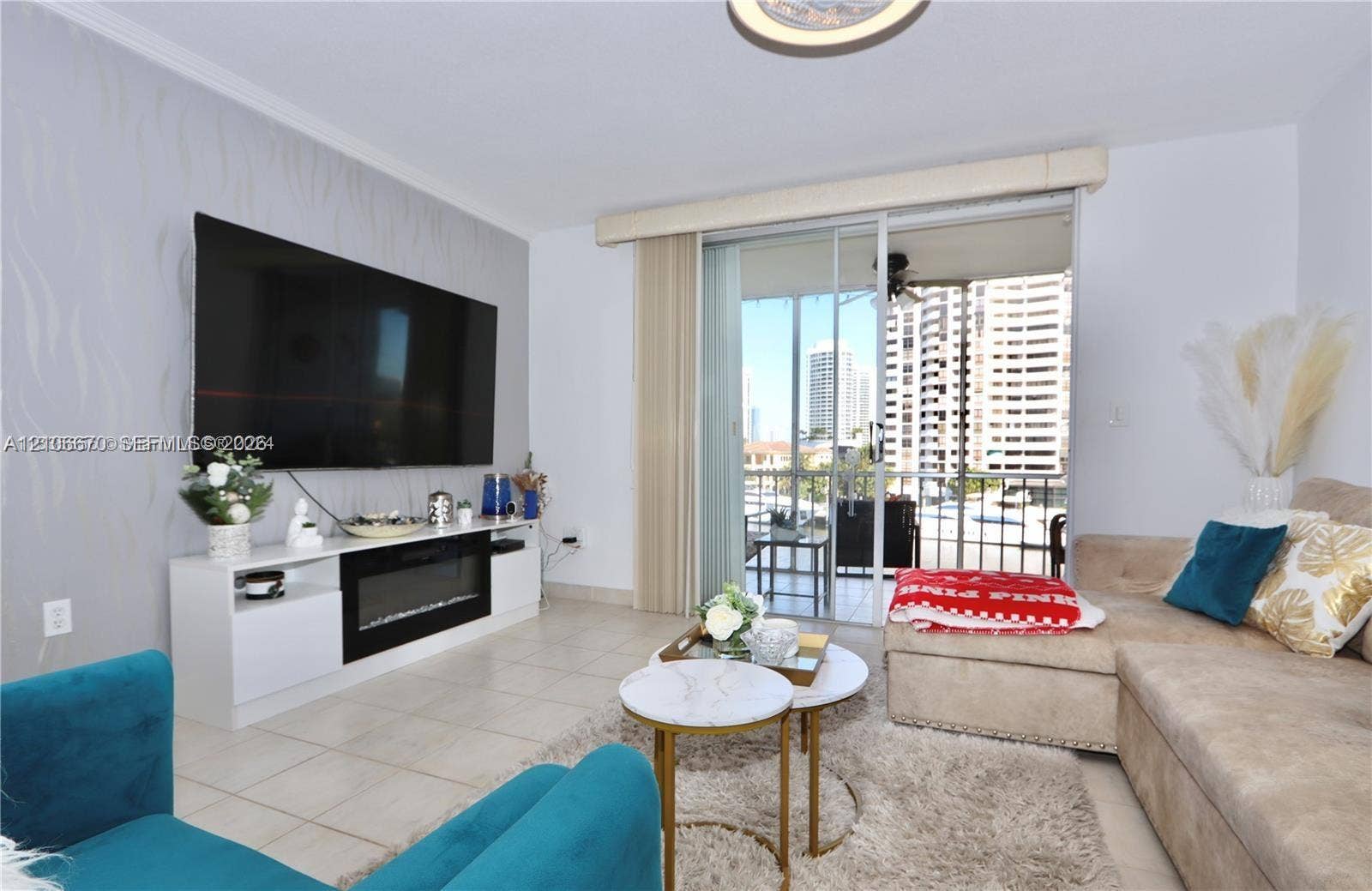 3030 Marcos Drive, #T512, Aventura, FL 33160 Living area featuring large-format tile flooring, textured accent wall, built-in media console with integrated electric fireplace, and sliding glass doors leading to a balcony
