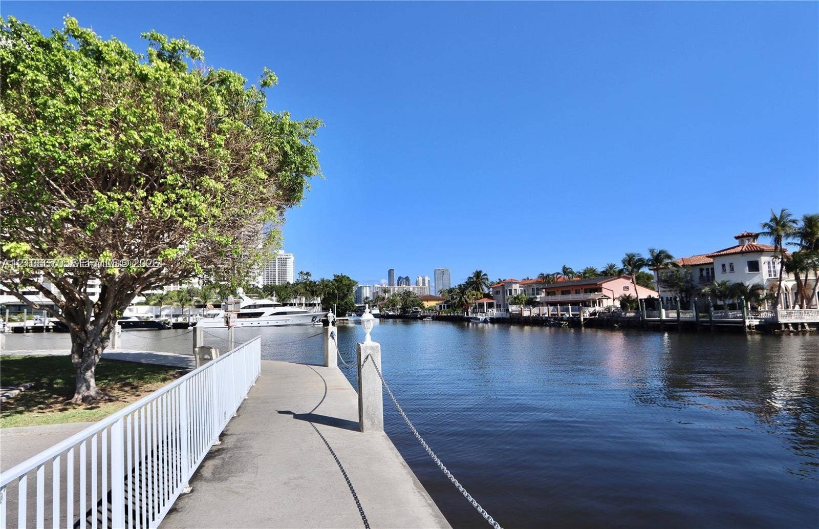 3030 Marcos Drive, #T512, Aventura, FL 33160 Waterfront walkway featuring metal railings, concrete paving, and mature trees