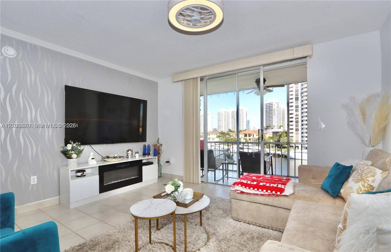 3030 Marcos Drive, #T512, Aventura, FL 33160 Living area featuring light-toned floor tiles, a floor-to-ceiling accent wall with patterned wallpaper, a built-in media console with an integrated electric fireplace, and sliding glass doors with access to a balcony