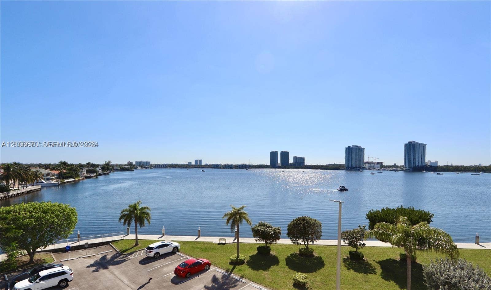 3030 Marcos Drive, #T512, Aventura, FL 33160 Waterfront setting featuring a bulkhead wall, landscaped lawn area, mature palm trees, and an expansive aquatic horizon