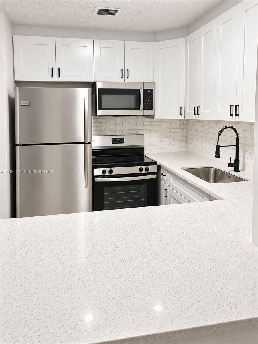 704 SE 2nd Avenue, #440, Deerfield Beach, Deerfield Beach, FL 33441 Kitchen featuring white shaker-style cabinetry, stainless steel appliances, quartz countertops, a white subway tile backsplash, and a matte black gooseneck faucet