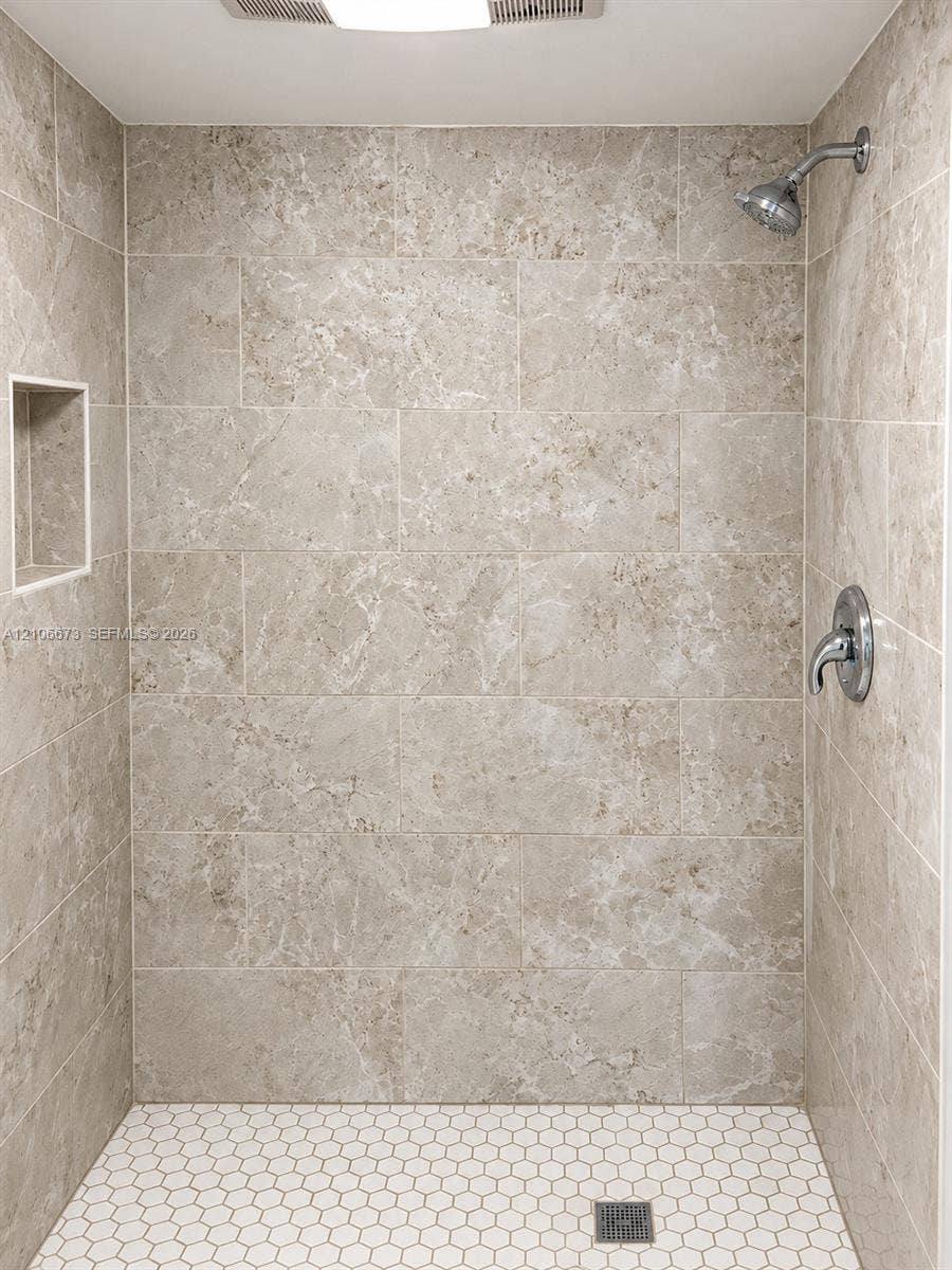 704 SE 2nd Avenue, #440, Deerfield Beach, Deerfield Beach, FL 33441 Walk-in shower featuring large-format neutral stone-finish wall tile, white hexagonal floor tile, chrome shower hardware, and a built-in recessed wall niche