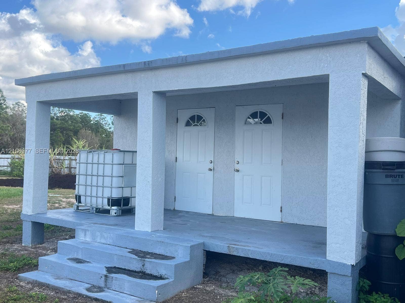 Detached structure with a stucco exterior, concrete porch, and dual entry doors featuring arched glass inserts