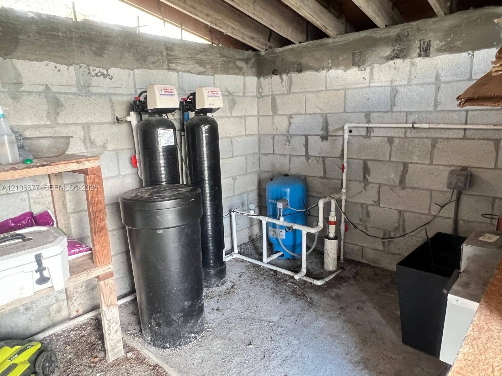 Utility area featuring concrete masonry unit walls, a dual-tank water treatment system, and a blue pressure tank